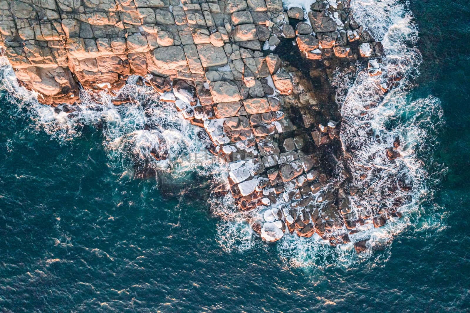Aerial top down view of an ocean blue waves breaking on the rocks