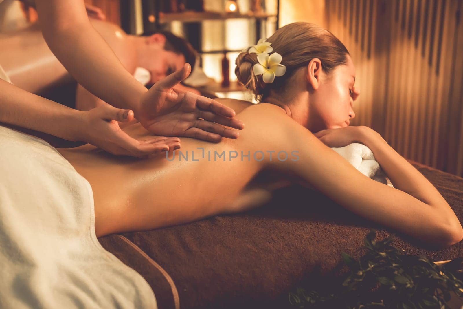 Caucasian couple customer enjoying relaxing anti-stress spa massage and pampering with beauty skin recreation leisure in warm candle lighting ambient salon spa at luxury resort or hotel. Quiescent