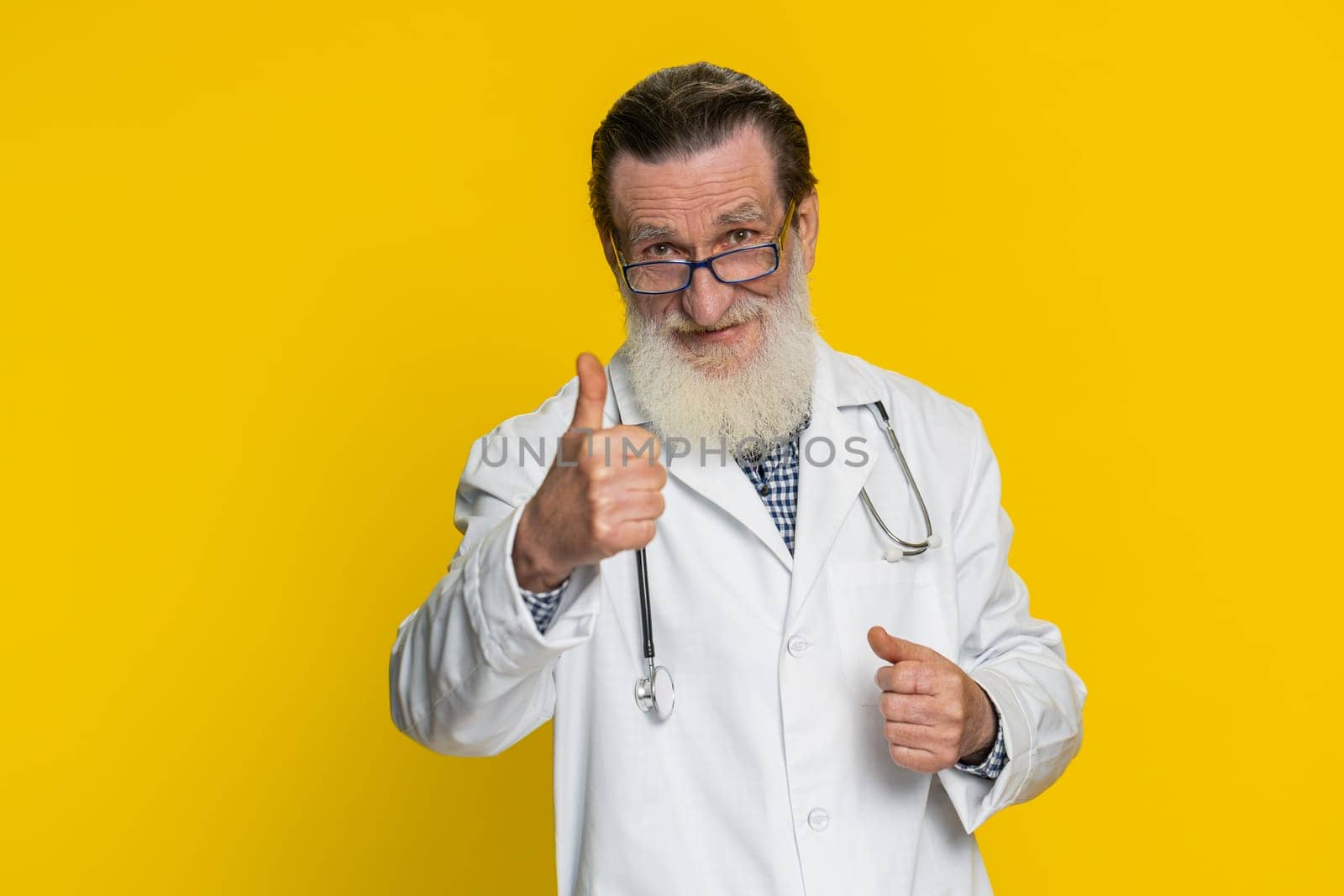 Like. Senior elderly doctor cardiologist man raises thumbs up agrees, gives positive reply good idea feedback celebrating success victory. Apothecary pharmacy grandfather isolated on yellow background