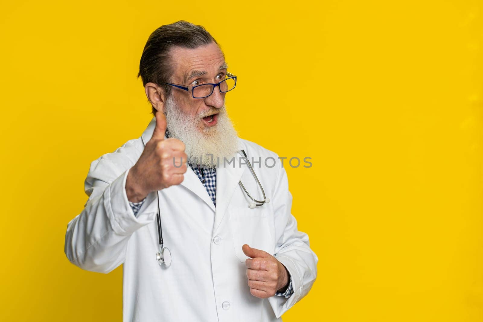 Like. Senior mature doctor cardiologist man raises thumbs up agrees, gives positive reply good idea feedback celebrating success victory. Apothecary pharmacy grandfather isolated on yellow background