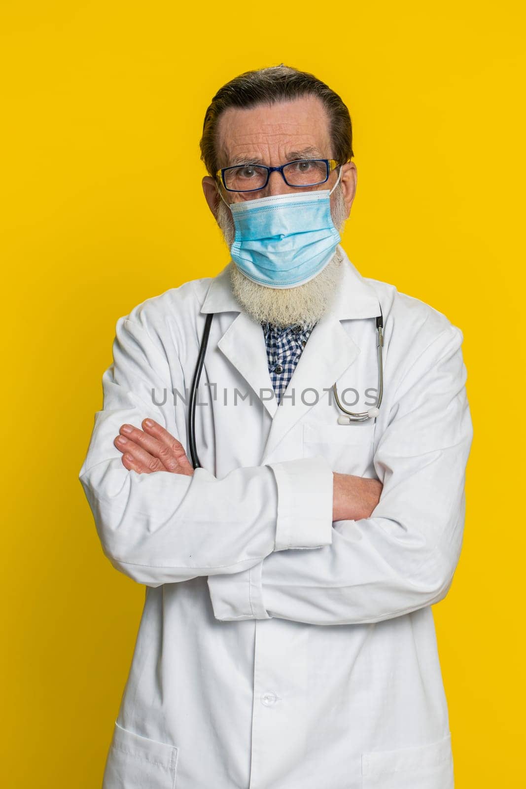 Happy senior doctor cardiologist man removing taking off medical protective mask. Flu treatment cure. Ending of pandemic quarantine. Apothecary pharmacy old grandfather on yellow background. Vertical