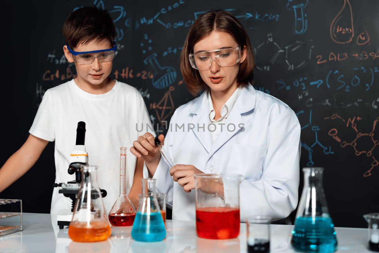 Teacher support schoolboy in laboratory. Schoolboy and teacher stand and experiment about science of chemistry in STEM class using liquid in glass container. Instructor mixing solution. Erudition.