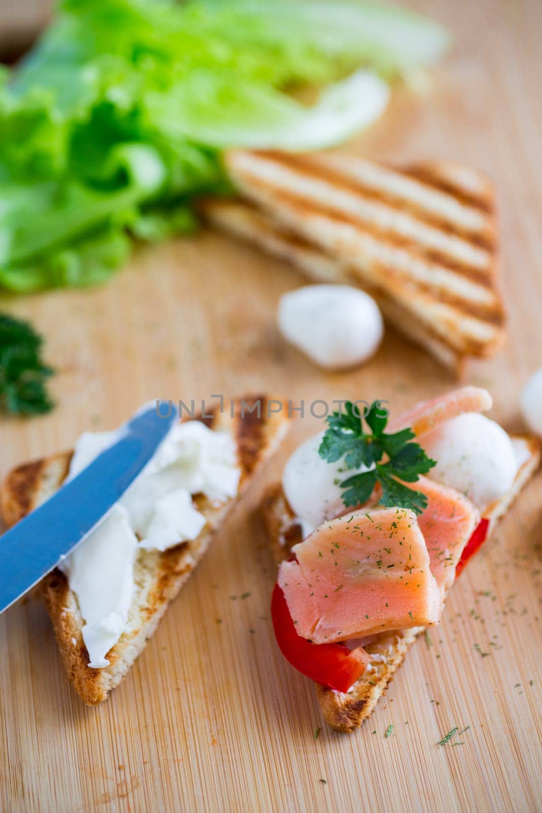 fried toast with salmon, cream cheese, salad, on a wooden table .