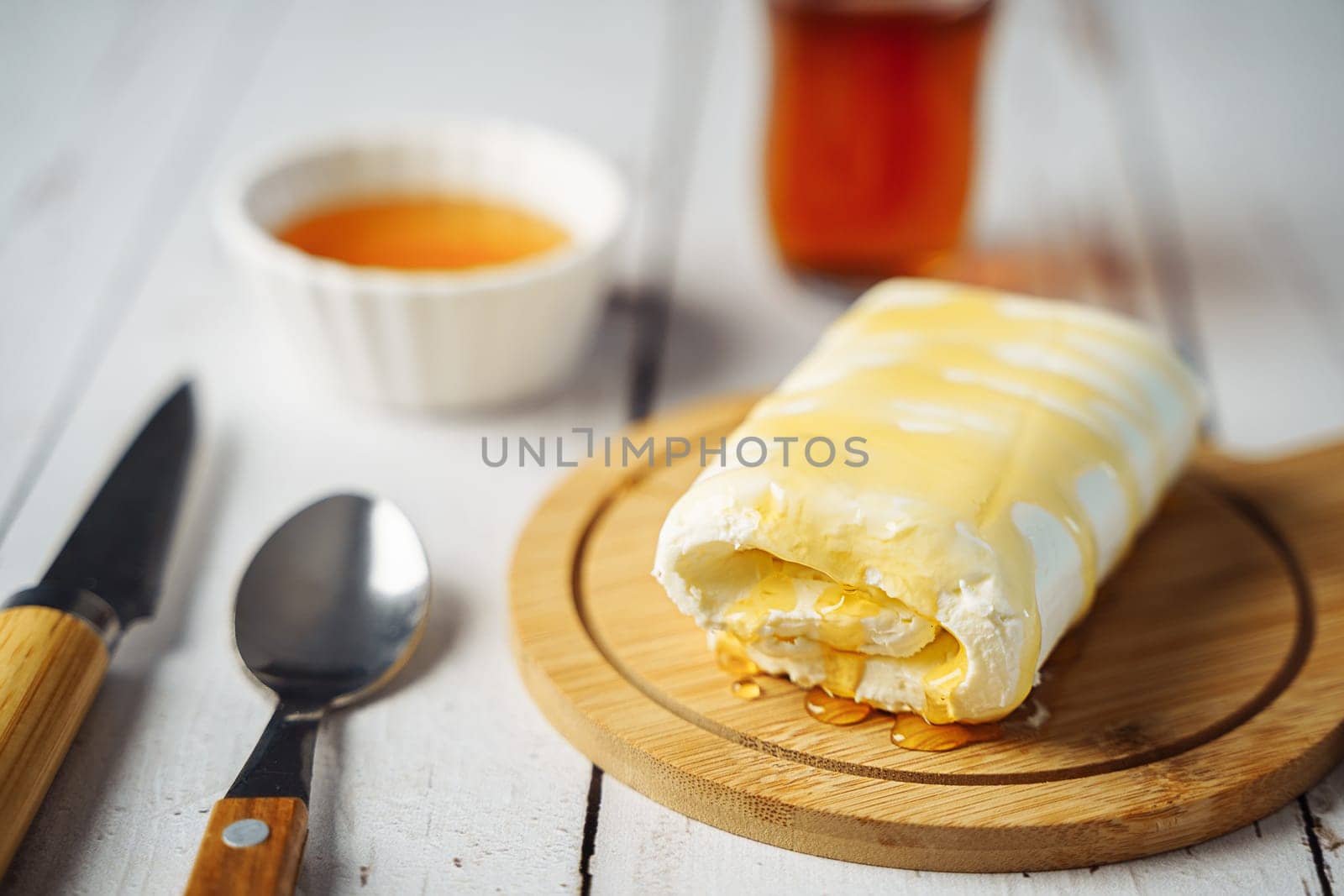 Close up picture of white cream milky kaymak butter roll poured with honey and tea on wooden plate by Ostanina