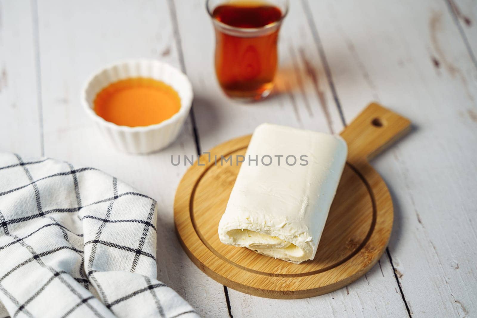 Close up picture of white cream milky kaymak butter roll poured with tea on wooden plate by Ostanina