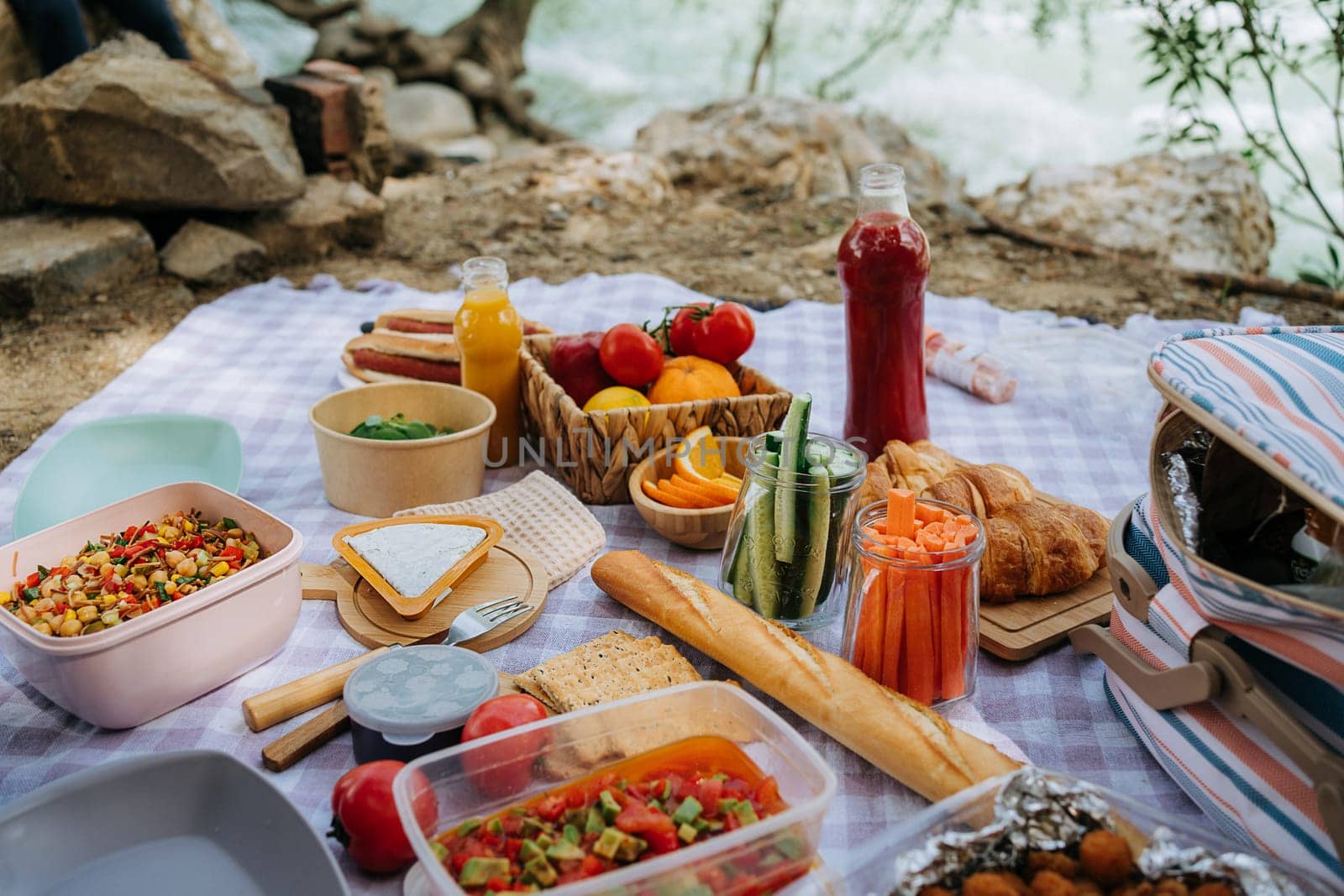 Picnic in the forest camping site with vegetables, juice, cheese, and croissants near mountain river. Fresh organic veggies surrounded with bread baguettes, salads by Ostanina