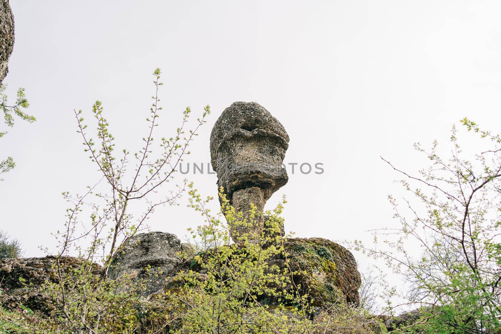 Head shape rock boulder standing on a mountain cliff. A hanging stone on the edge of rocky barrow. by Ostanina