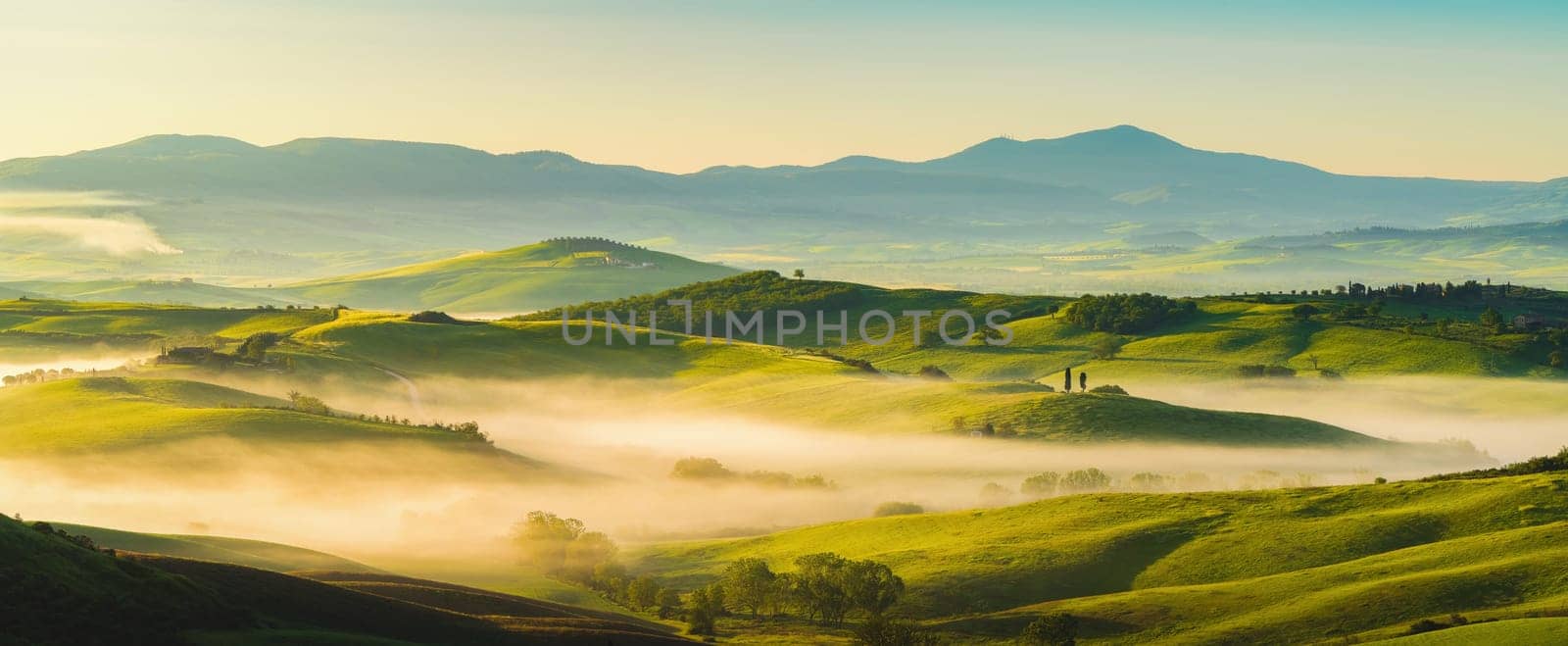 House surrounded by cypress trees among the misty morning sun-drenched hills of the Val d'Orcia valley at sunrise in San Quirico d'Orcia, Tuscany, Italy