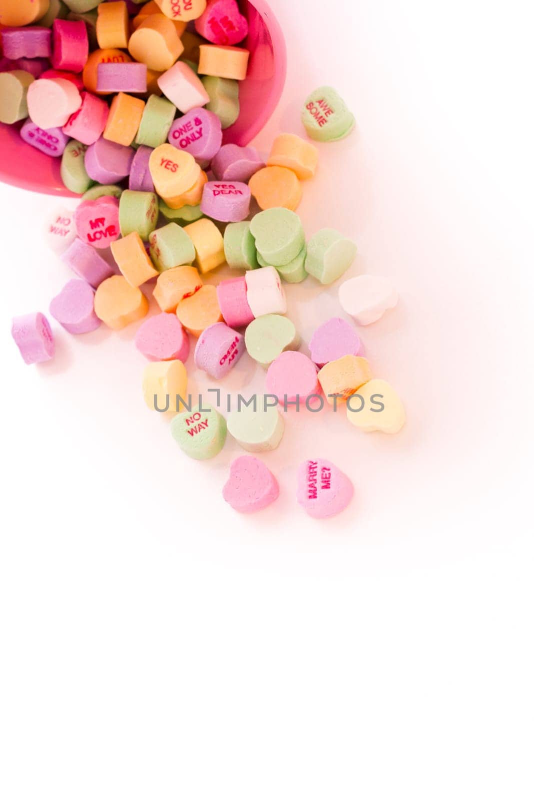 Conversation heart candies spilled from pink bucket.