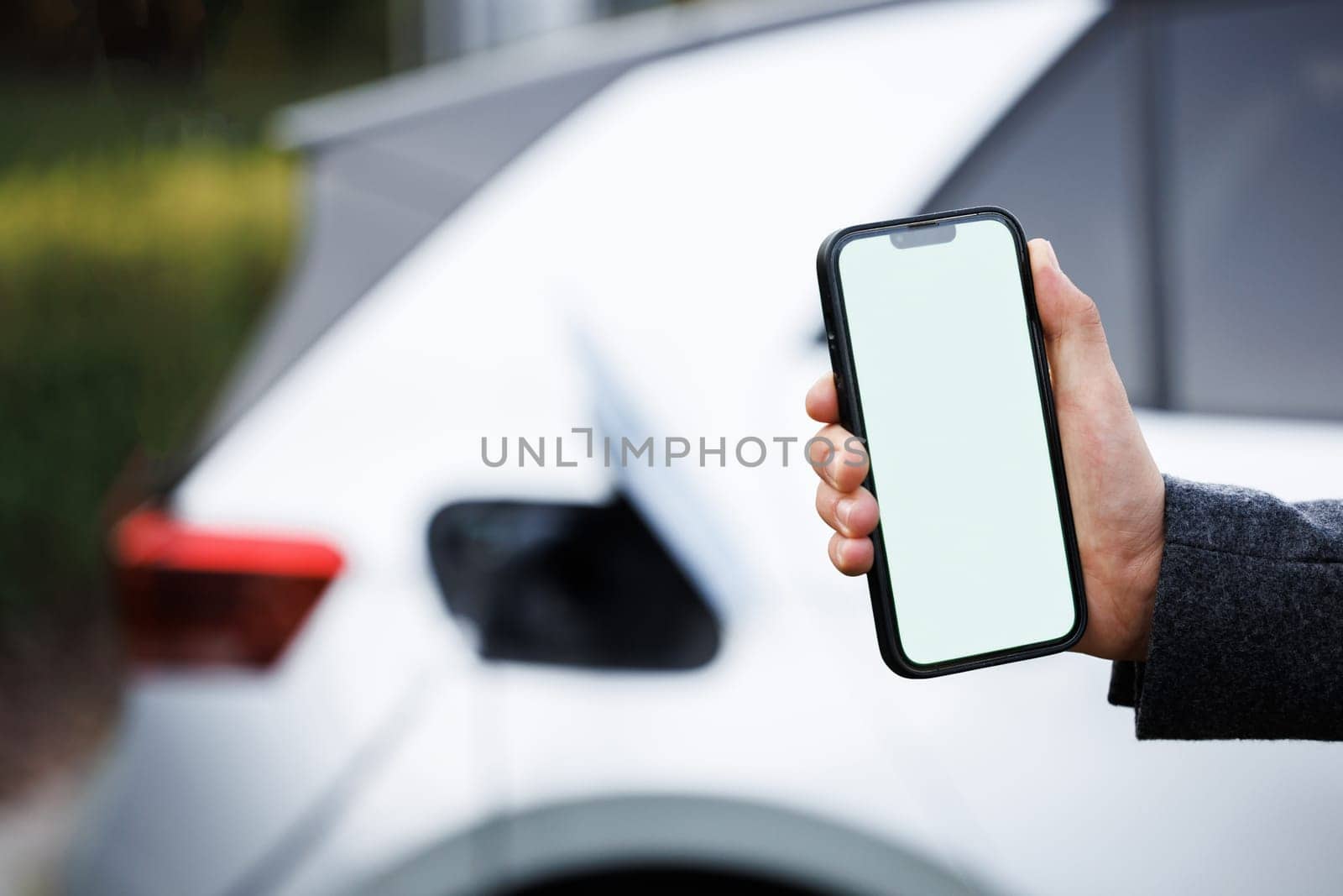 Process of charging is showing on smartphone. Close up view of man with his electric car. Man holding smartphone while charging car at electric vehicle charging station, closeup by uflypro