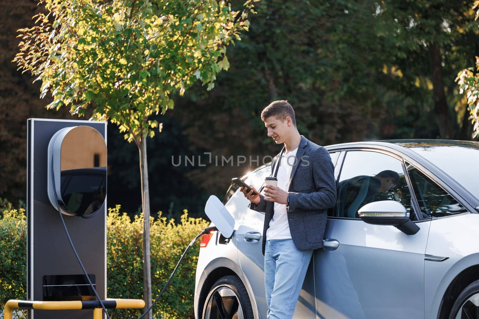 Businessman using smartphone and waiting power supply connect to electric vehicles for charging the battery in car. Plug charging an Electric car from charging station.