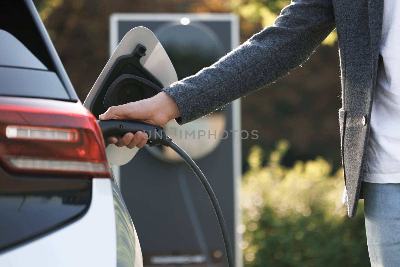 The driver of the electric car inserts the electrical connector to charge the batteries. Unrecognizable man attaching power cable to electric car. Electric vehicle Recharging battery charging port.