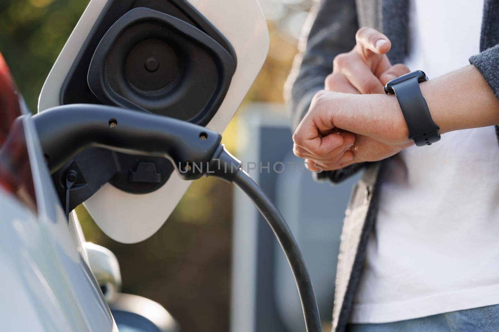 Businessman plugging in charging cable to to electric vehicle. Male hand inserts power connector into EV car and charges batteries, uses smartwatch for activates start charging by uflypro