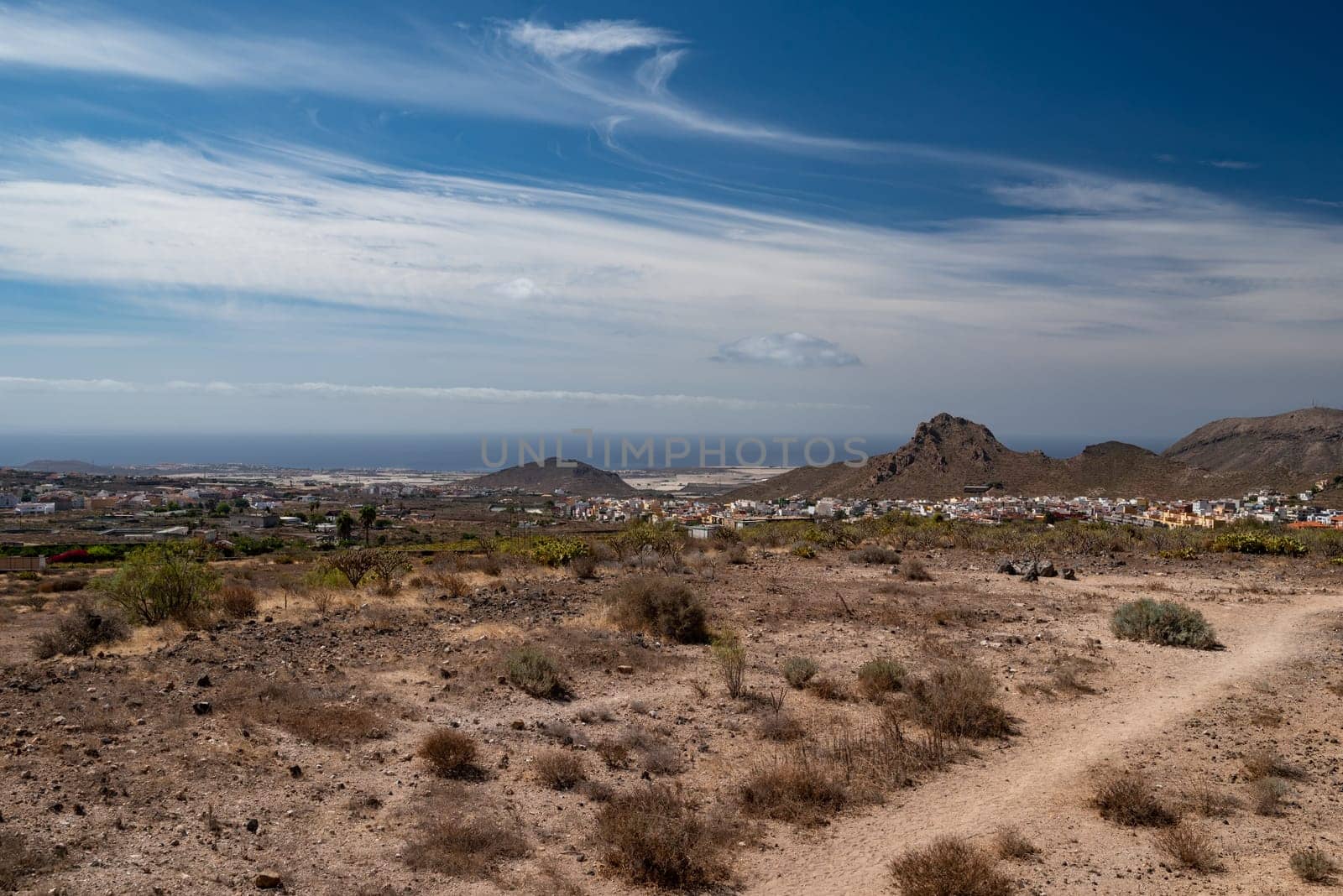 Hiking trail in a desert with a view of a city, sea or ocean and mountains by amovitania