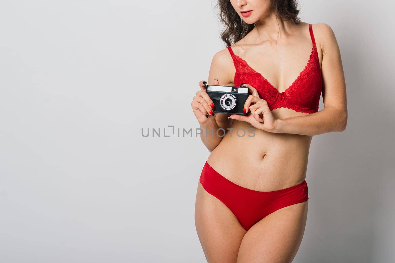 Beautiful female with pretty smile in red lingerie pinup style holding photo camera, isolated on white