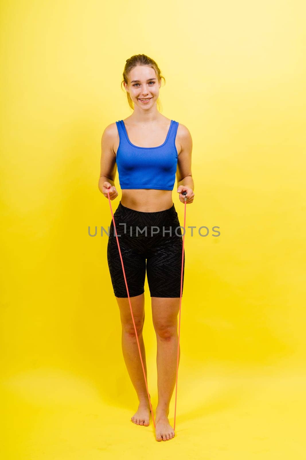 Portrait of gentle muscular woman holding skipping rope on her neck over yellow background