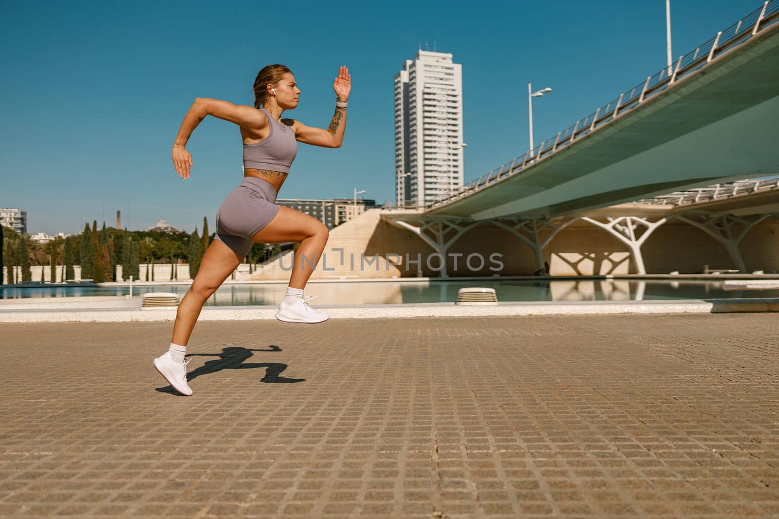 Young woman in sportswear is running on modern buildings background. Active lifestyle concept by Yaroslav_astakhov