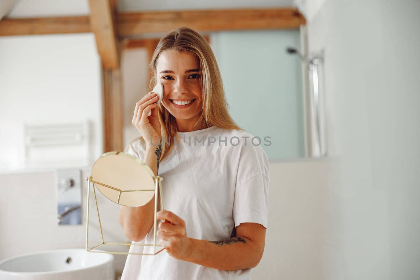 Young woman removing makeup with cotton pad in front of mirror standing in bathroom