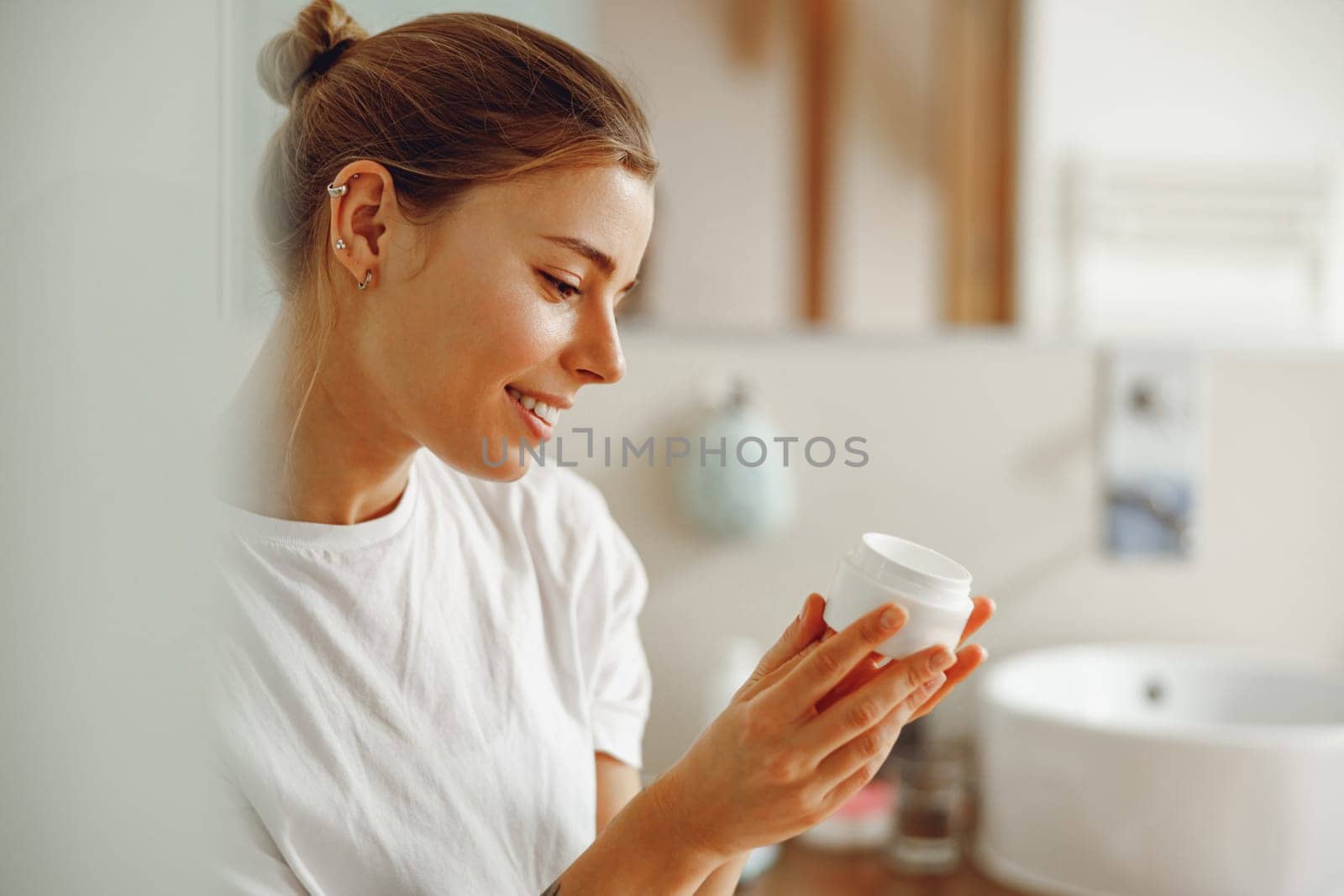 Smiling woman holding jar with skincare cream in hands. Home beauty routine