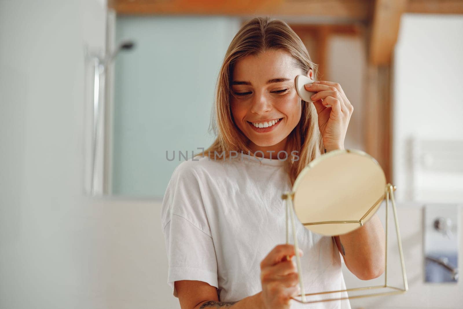 Smiling woman wiping her face with cotton pad in the bathroom. Skin care concept