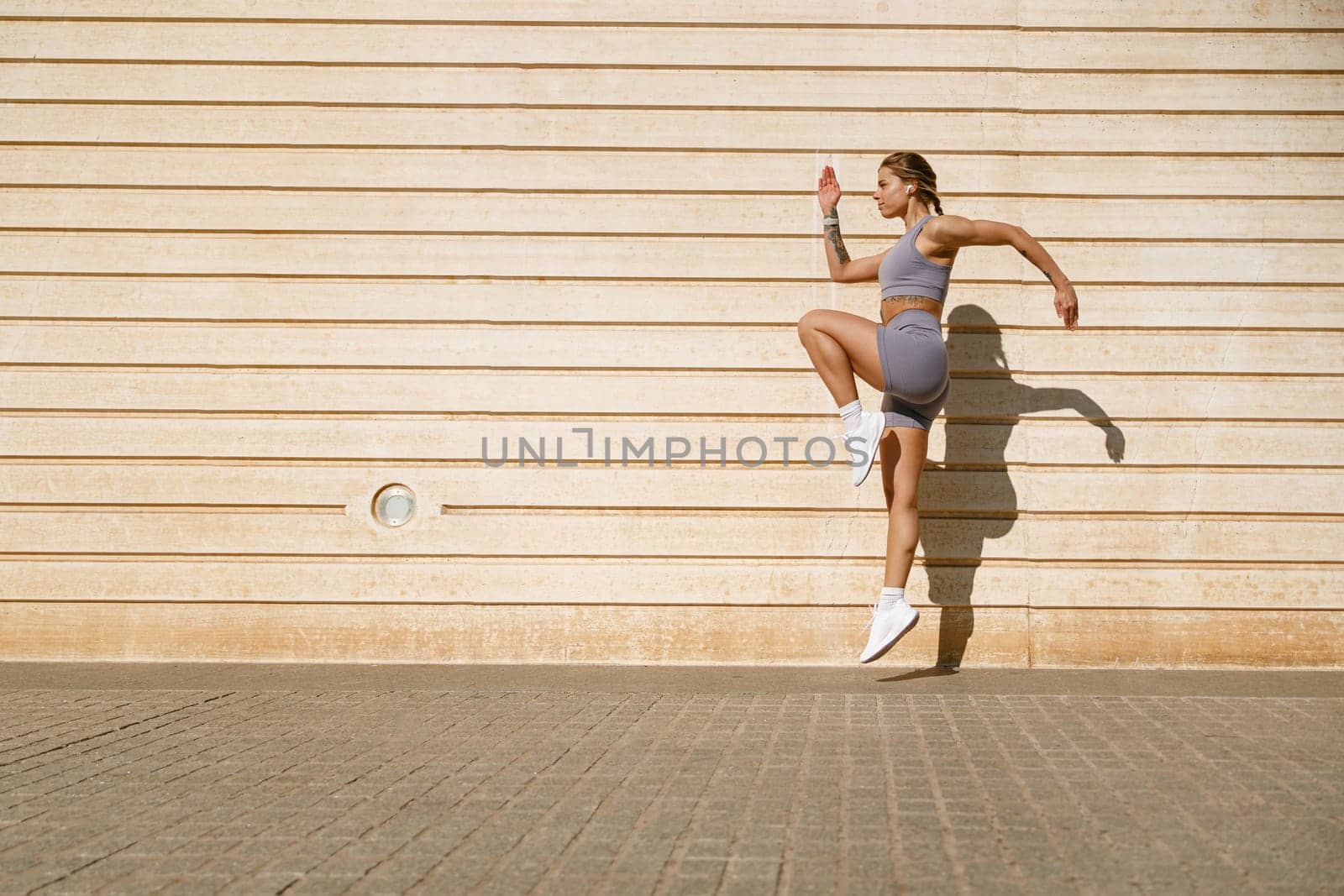 Young fit woman in sportswear leaping in the air with wall backdrop outdoors. High quality photo by Yaroslav_astakhov