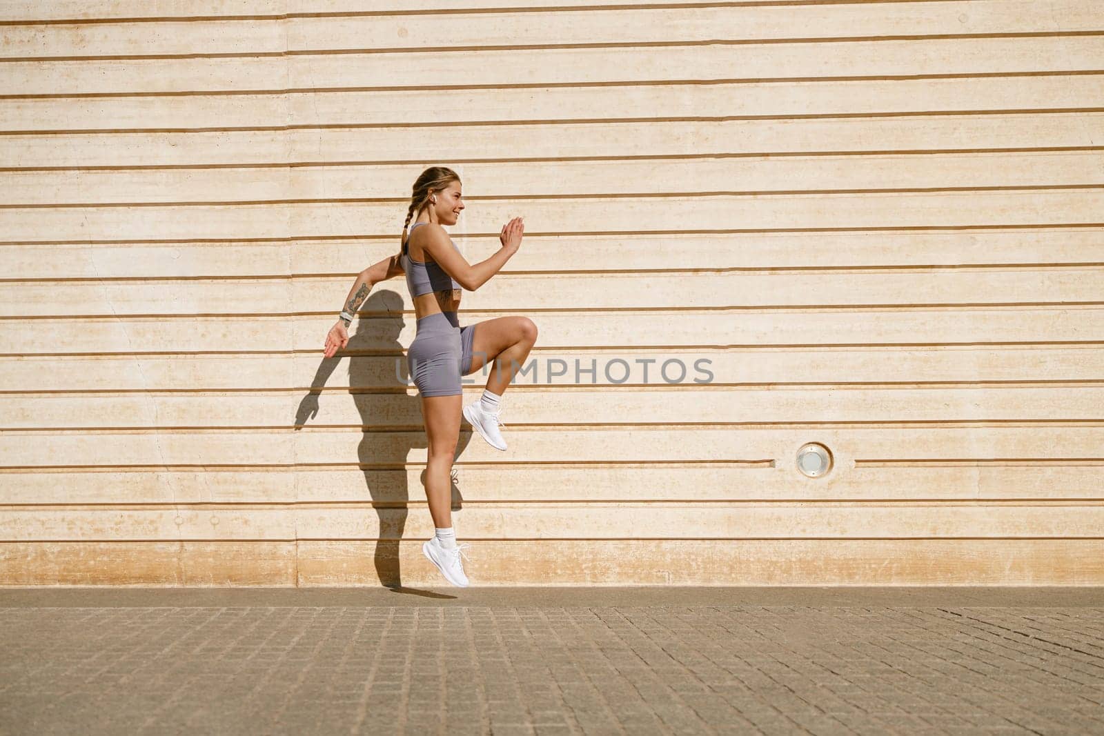 Young fit woman in sportswear leaping in the air with wall backdrop outdoors. High quality photo