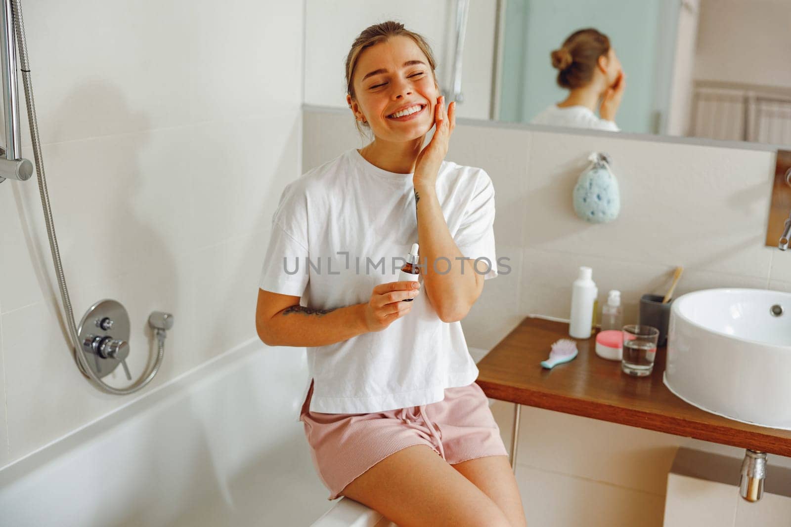 Beautiful young woman applying cosmetic serum onto her face in bathroom. Facial Skincare by Yaroslav_astakhov