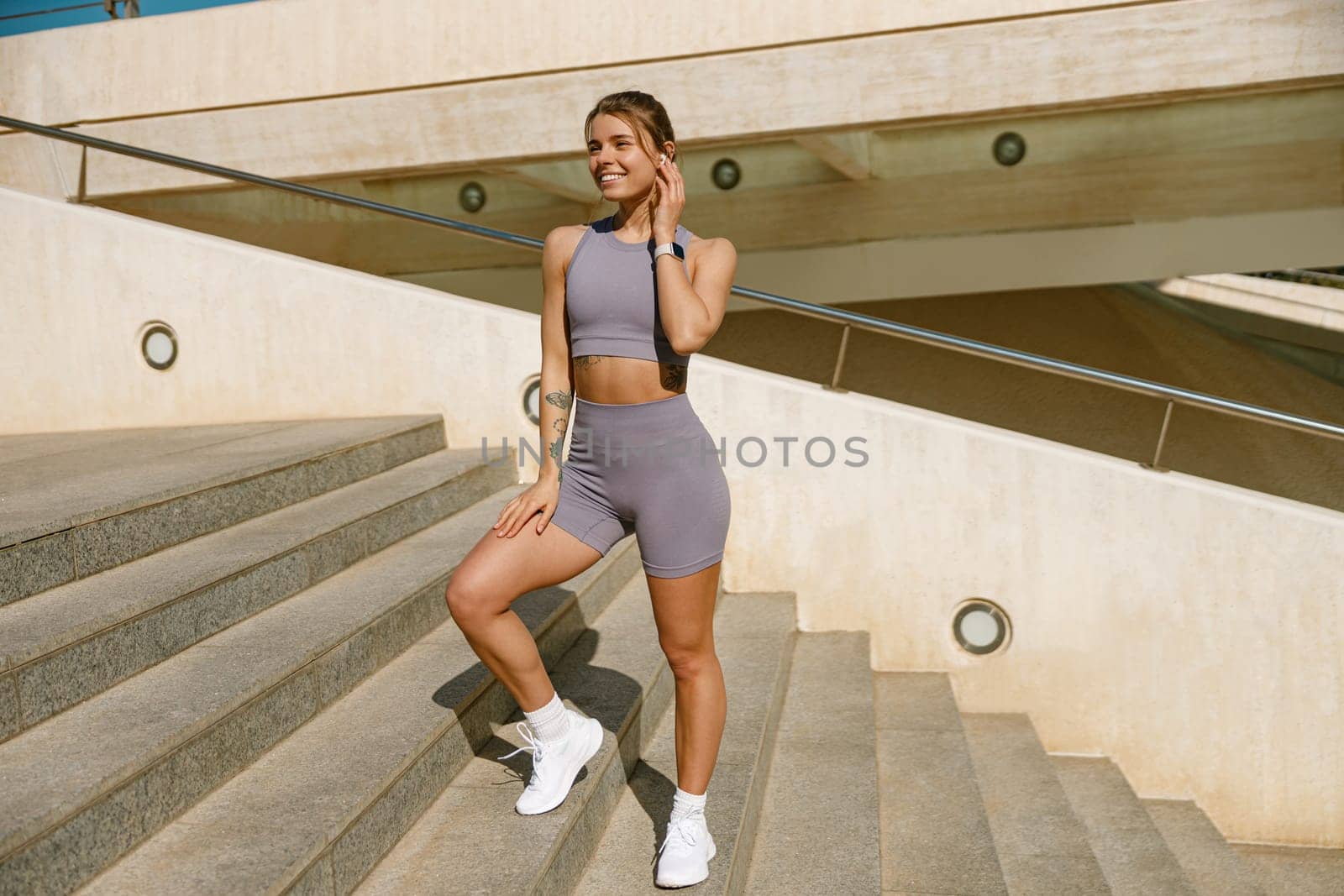 Smiling woman in sportswear have a rest after workout outside standing on bridge background by Yaroslav_astakhov