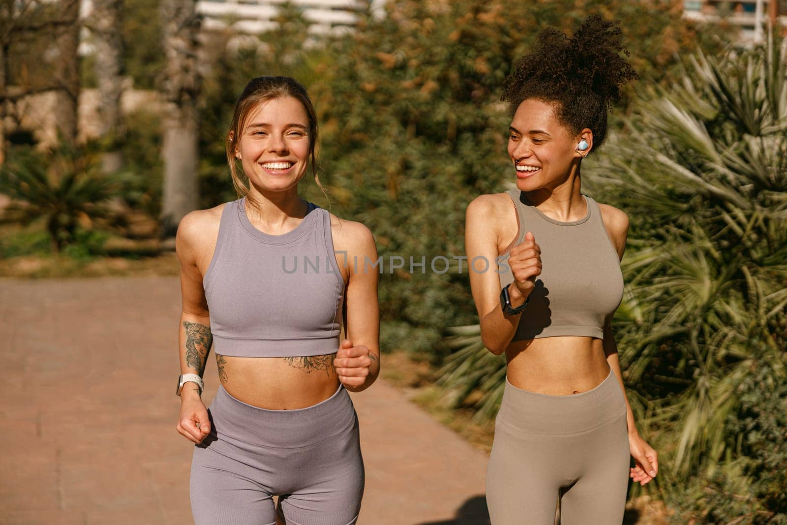 Two young women in sportswear are running on public park background. Active lifestyle concept