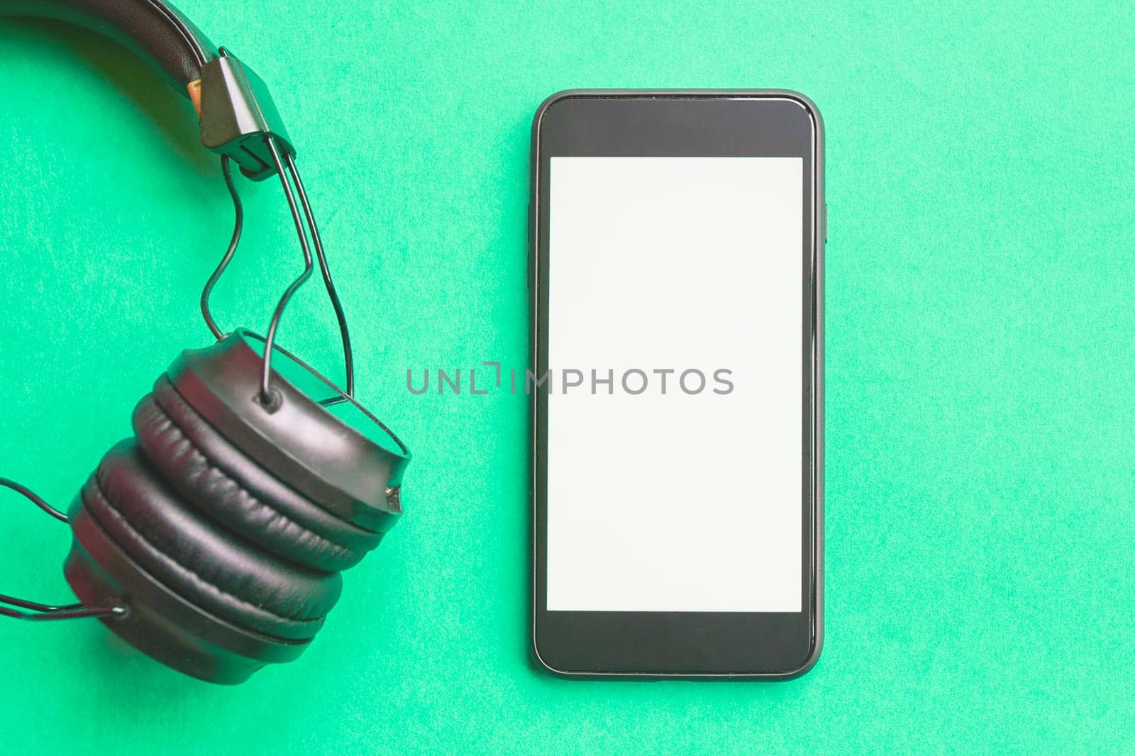 Headphones and smartphone on colorful background. Flat lay concept: headphones and telephone on green pastel backgrounds.