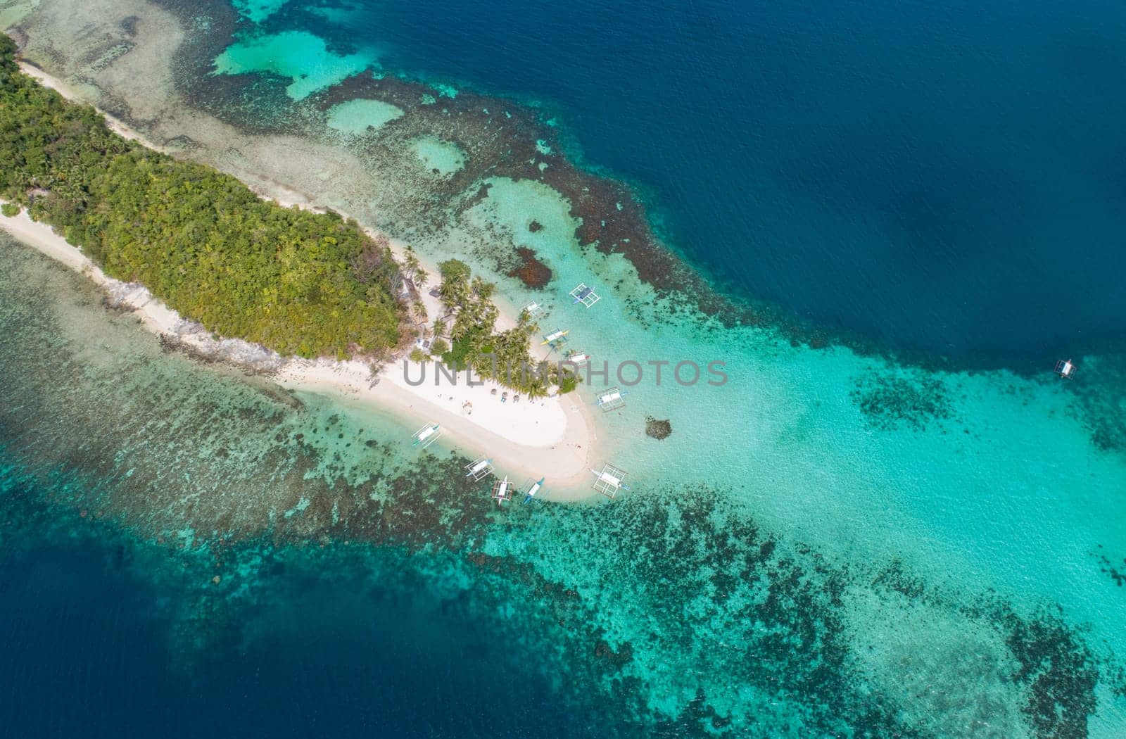 Aerial view of sandy beach on a tropical island with palm trees by coral reef atoll.