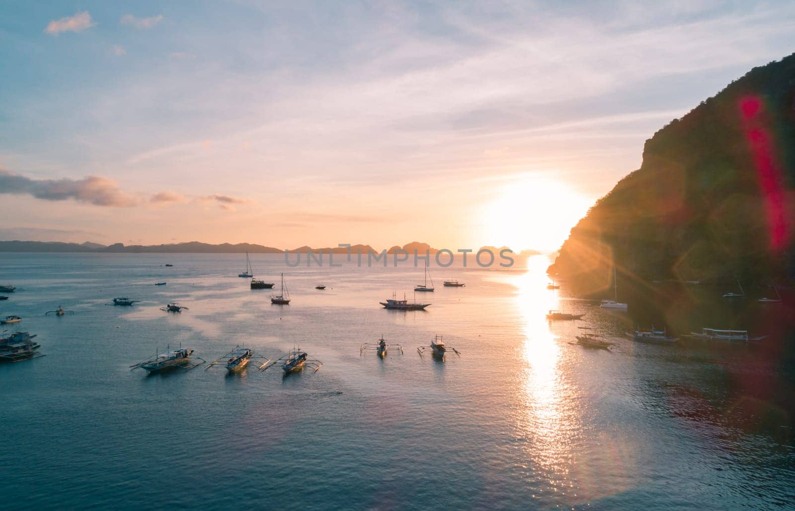 Aerial view of cliffs in the sea, yachts are sailing nearby, mountains covered with tropical forest. Aerial view of the gorgeous tropical mountains and the ocean.