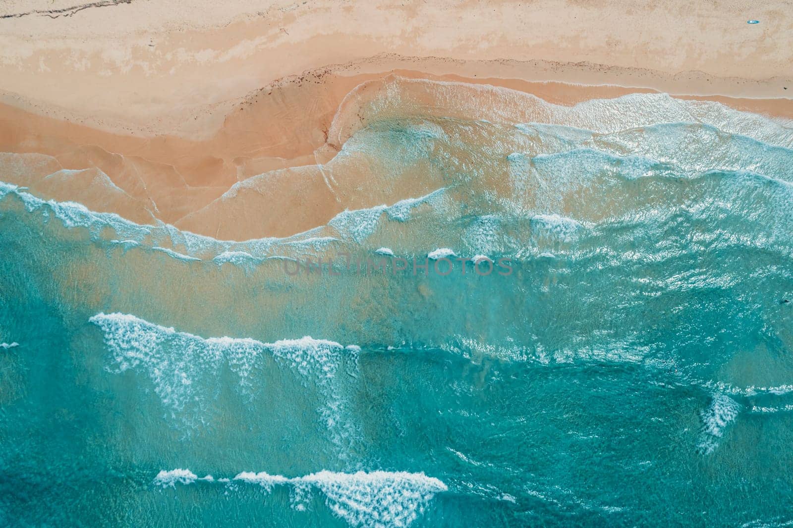 Aerial top view of turquoise ocean wave reaching the coastline.