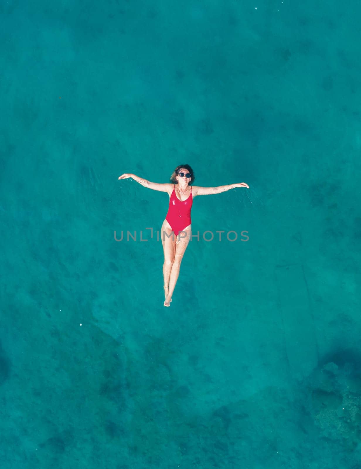 Aerial View of a Woman in Red Swimsuit Floating Serenely on the Crystal Clear Ocean Waters During Midday by Busker
