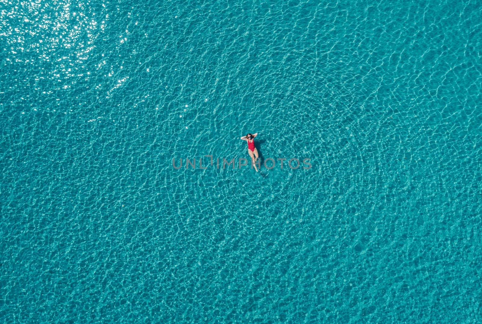 Aerial View of a Woman in Red Swimsuit Floating Serenely on the Crystal Clear Ocean Waters During Midday