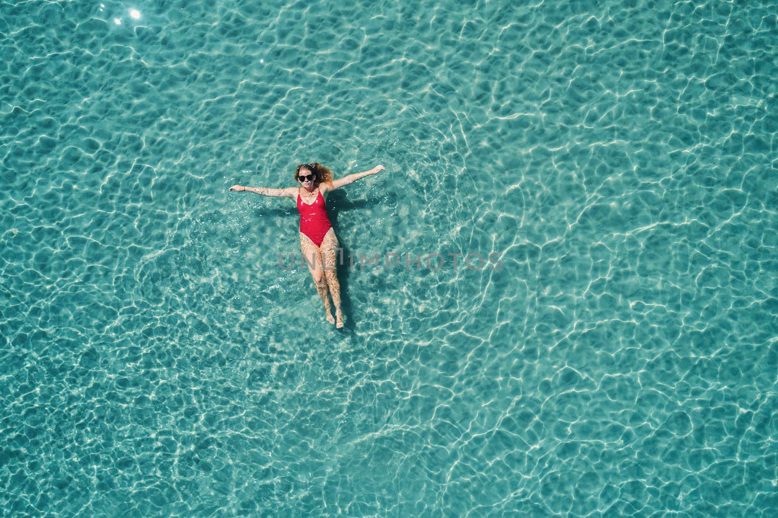 Aerial View of a Woman in Red Swimsuit Floating Serenely on the Crystal Clear Ocean Waters During Midday