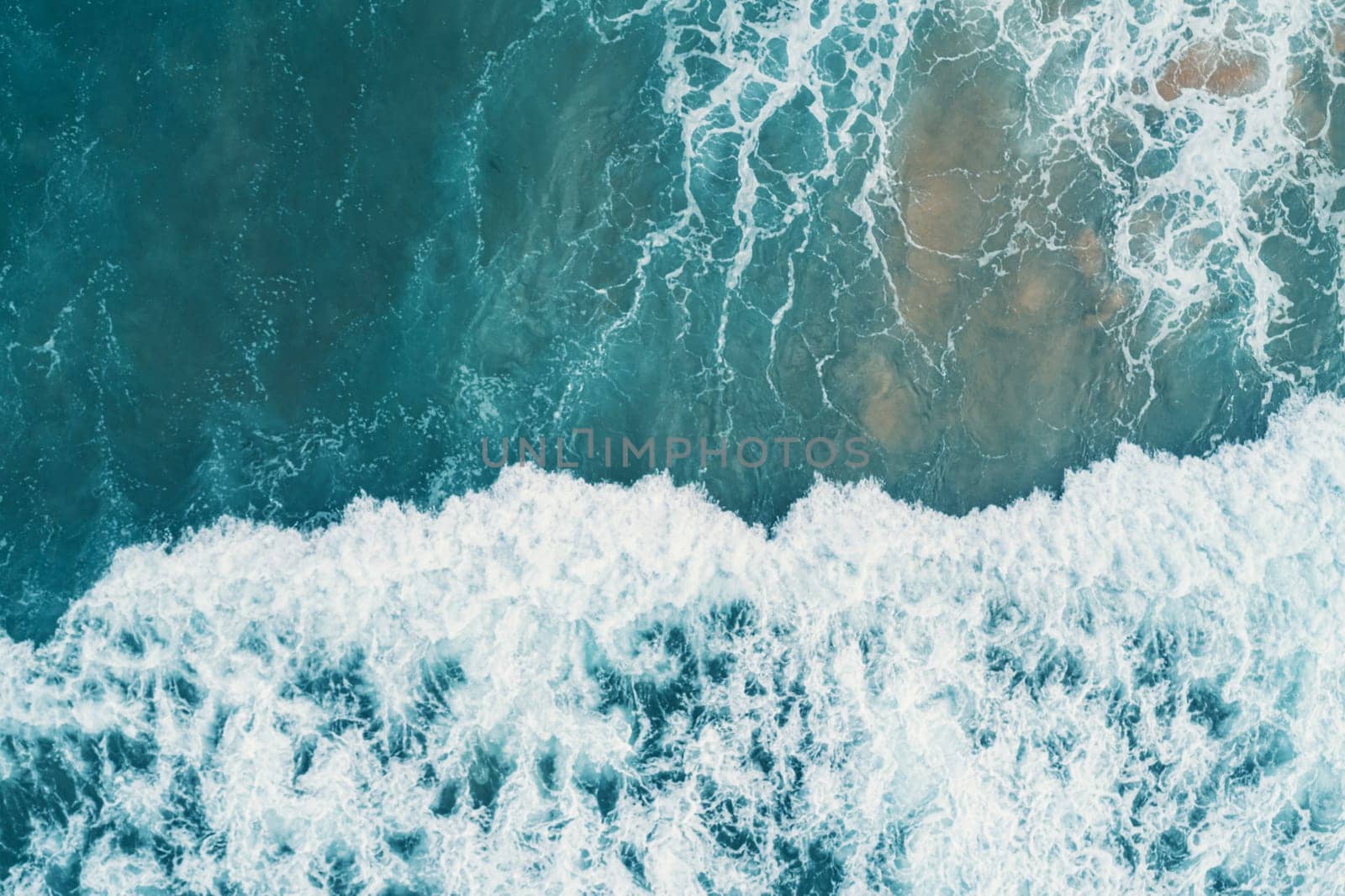 Aerial view of white foam on the surface of the blue sea.