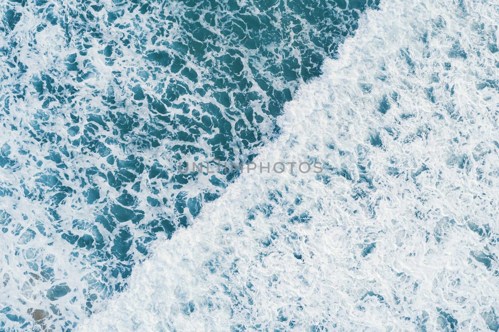 Aerial view of white foam on the surface of the blue sea.