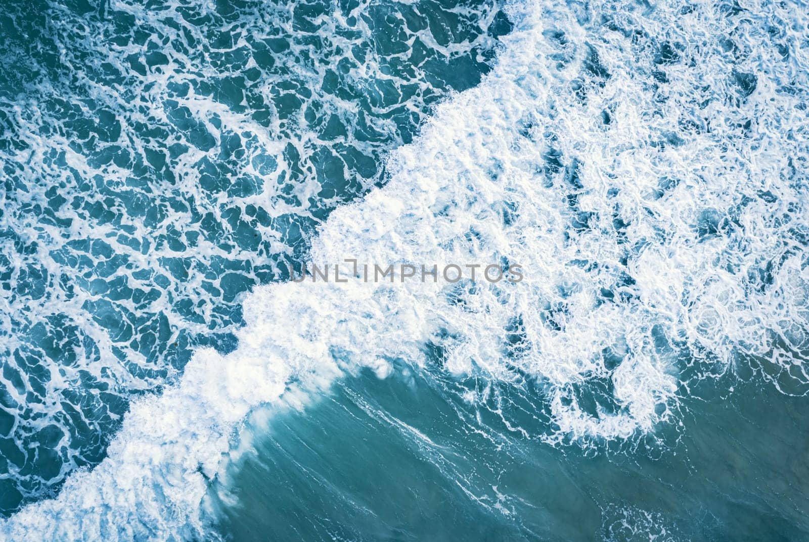 Aerial view of white foam on the surface of the blue sea.