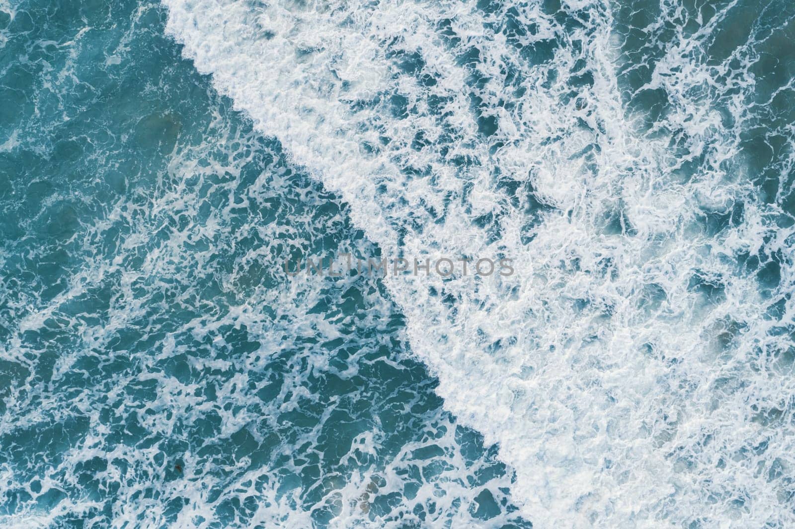 Aerial view of white foam on the surface of the blue sea.