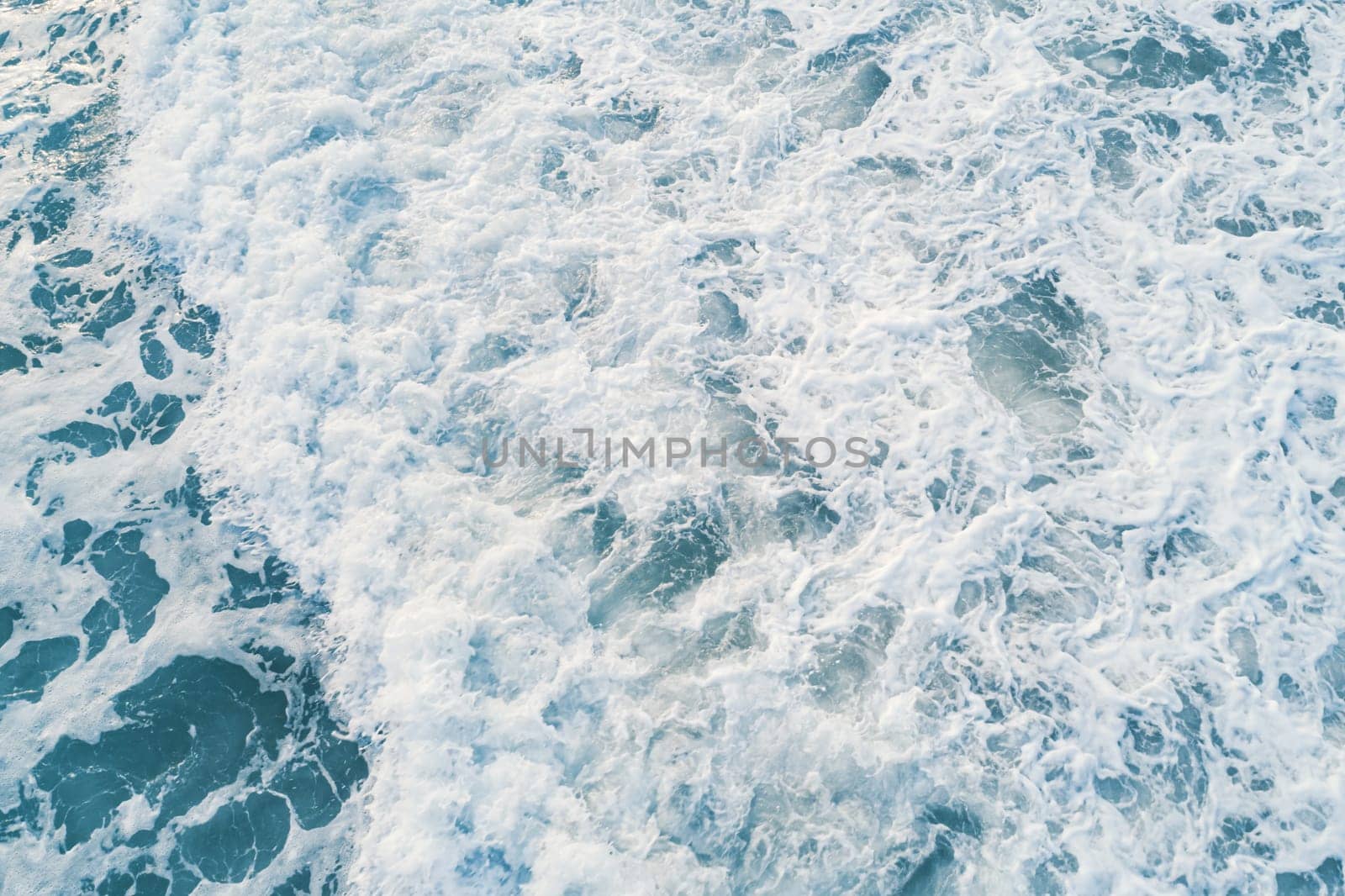 Aerial view of white foam on the surface of the blue sea.