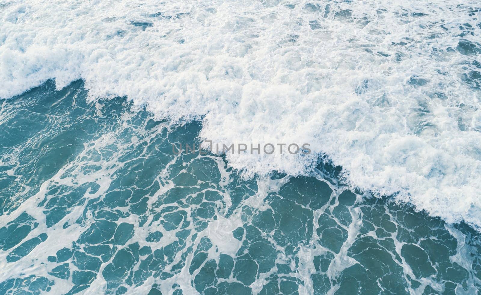 Aerial view of white foam on the surface of the blue sea.