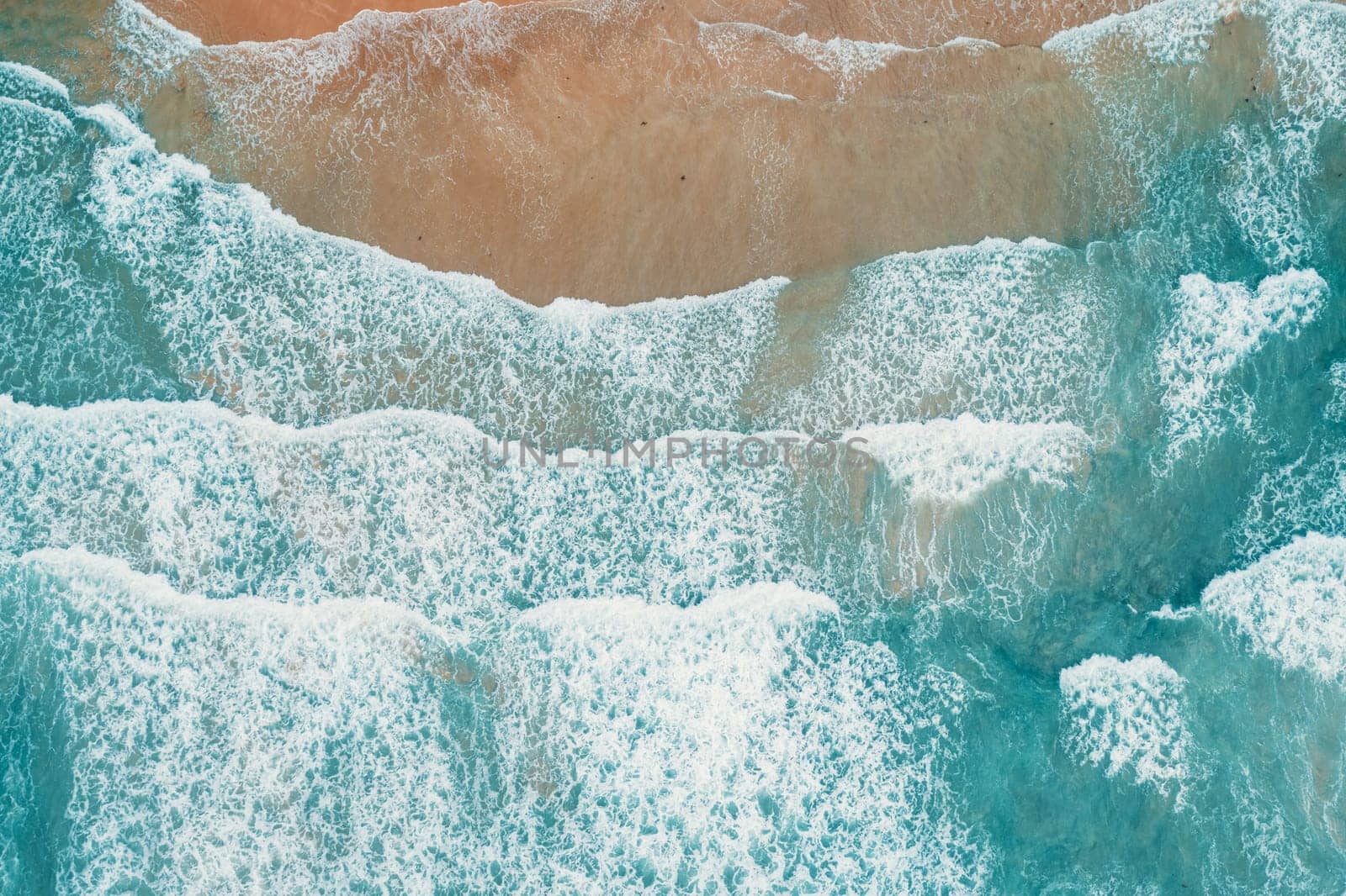 Aerial top view of turquoise ocean wave reaching the coastline.