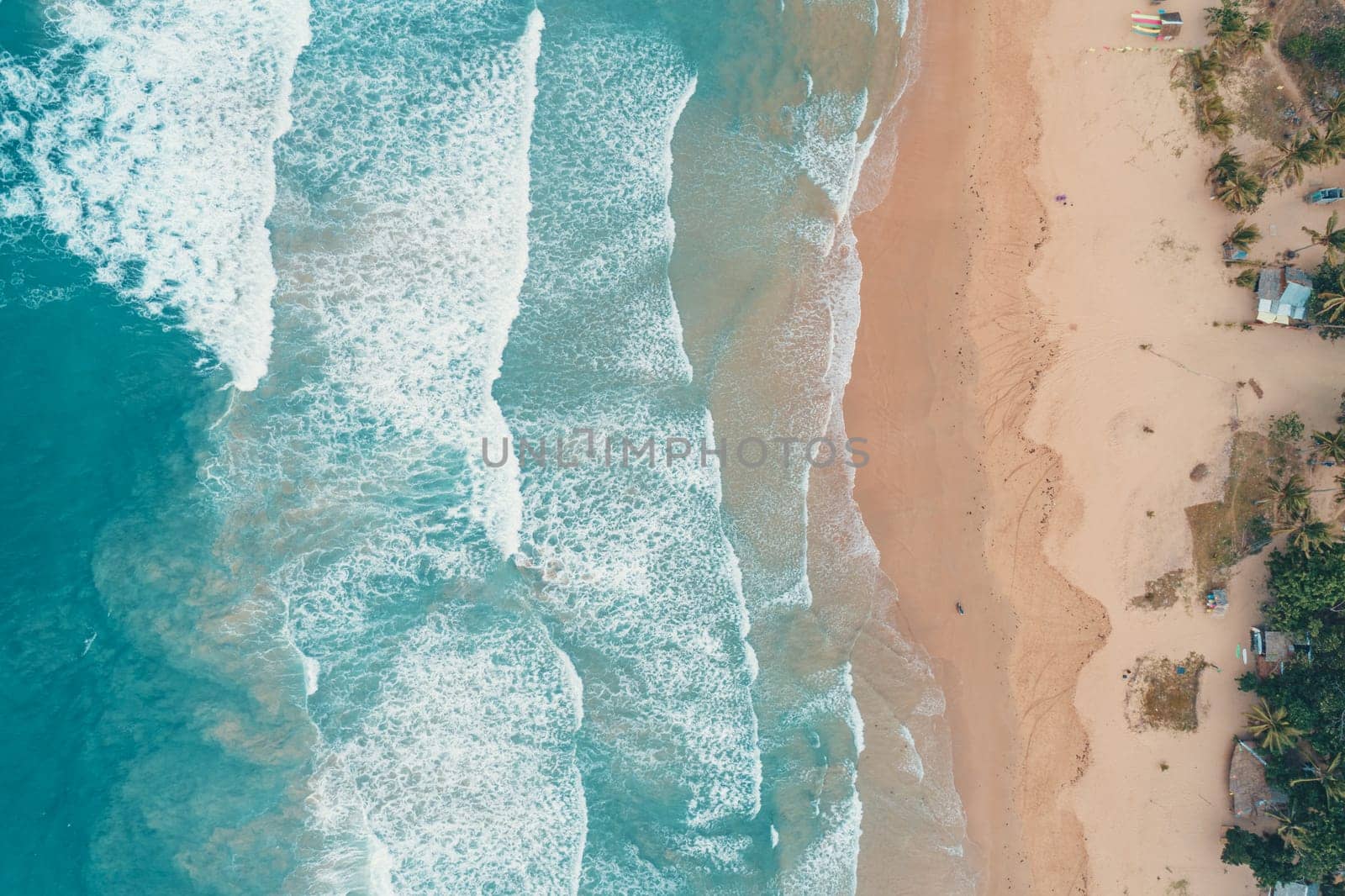 Aerial top view of turquoise ocean wave reaching the coastline.