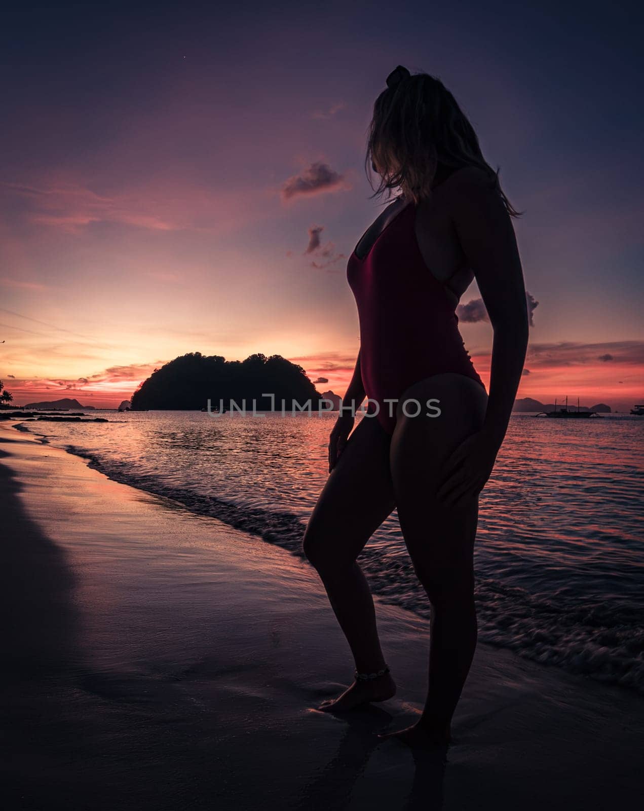 Serene sunset silhouette of a woman standing on a beach during twilight by Busker