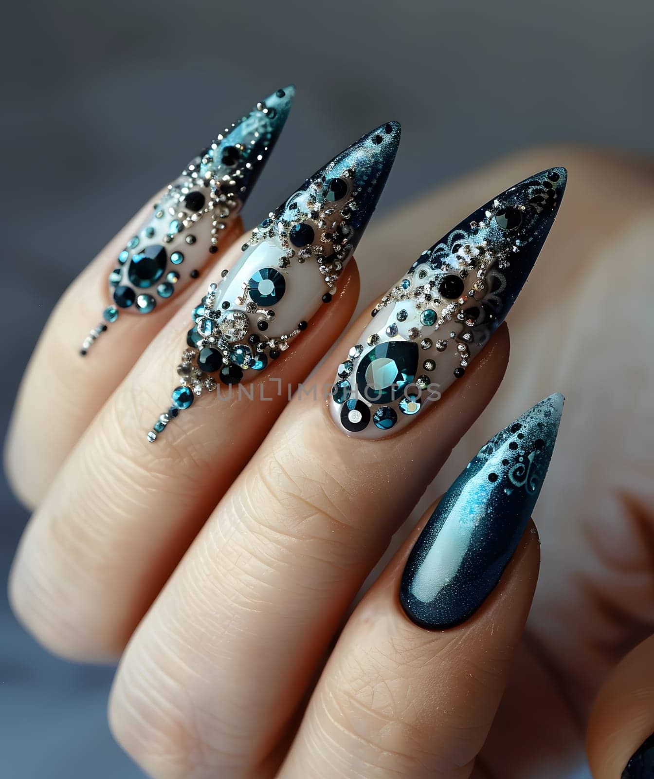 A closeup of a womans hand featuring long nails adorned with rhinestones. The nails are painted with liquid nail polish, enhancing their natural beauty