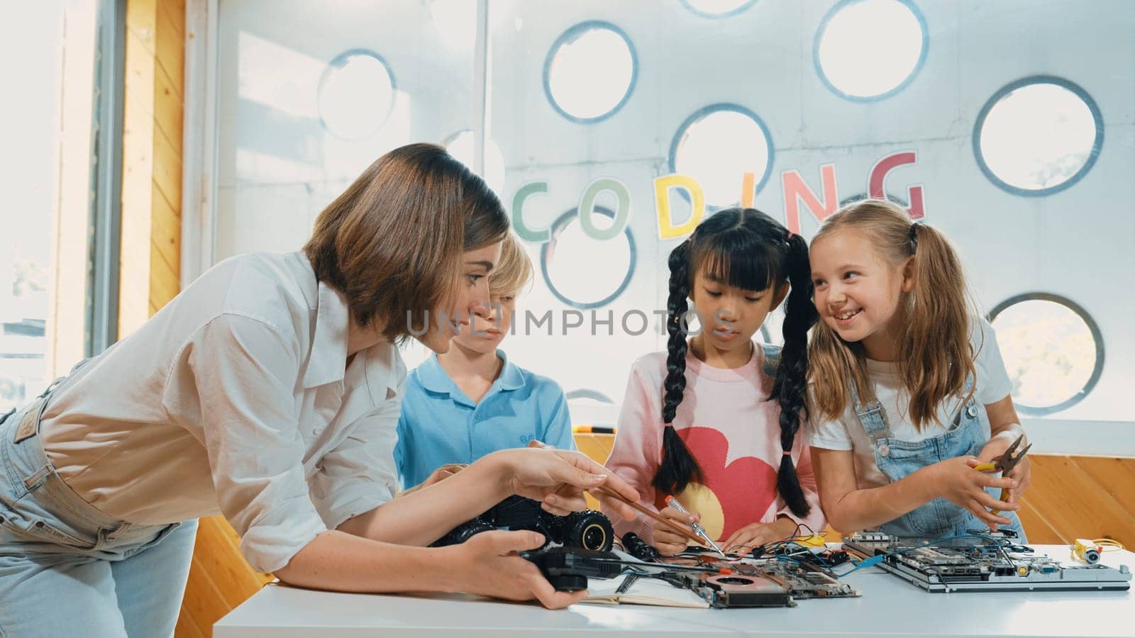 Young smart caucasian teacher teaching diverse students about electronic board. Multicultural children learn about digital electrical tool and fixing motherboard by using chips and wires. Erudition.