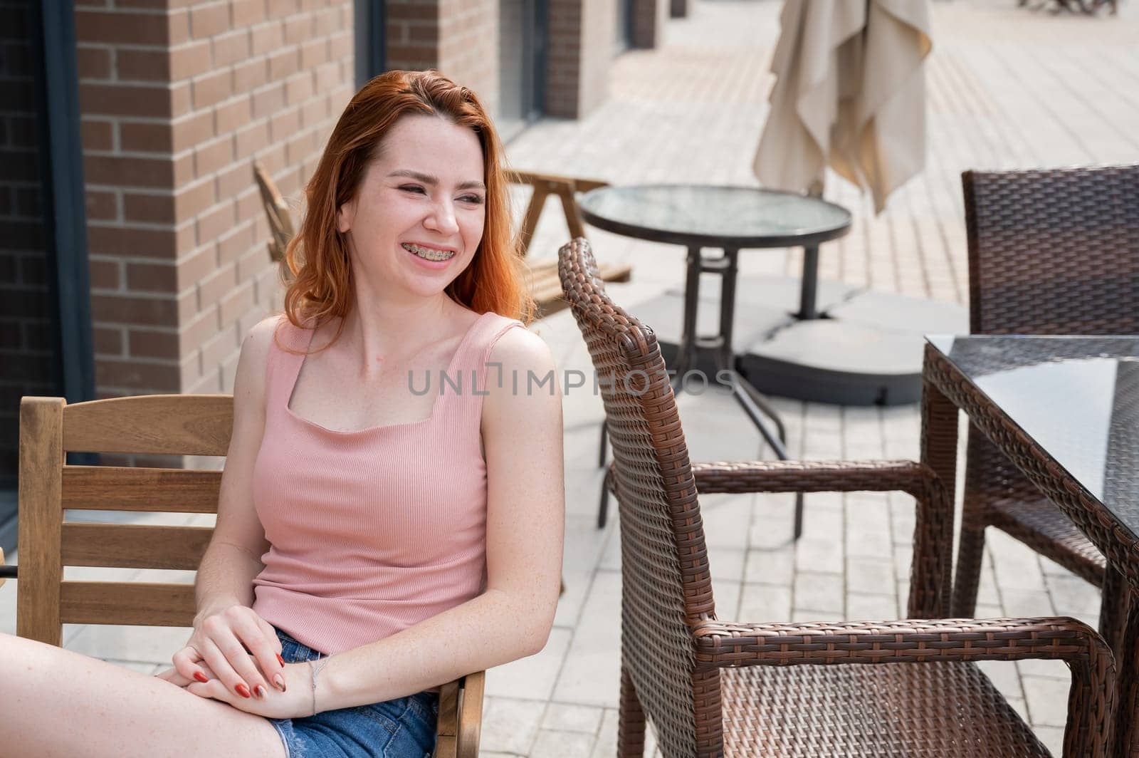 Beautiful young red-haired woman with braces on her teeth smiling while sitting in an outdoor cafe