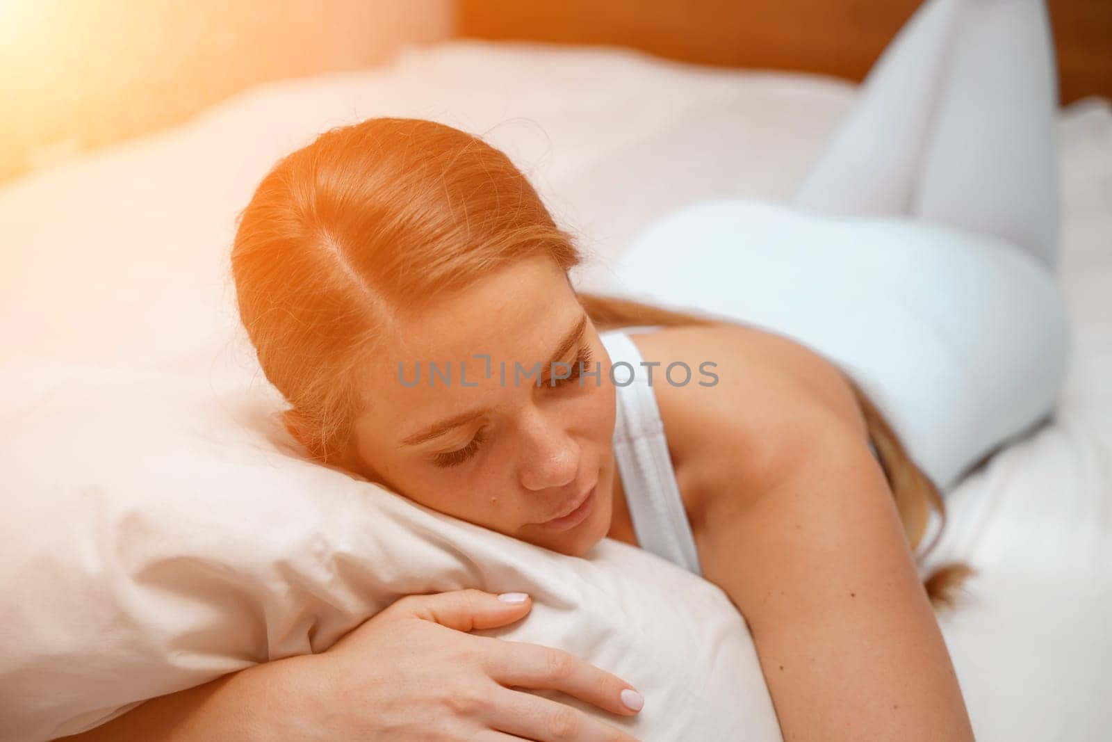 A young woman lies on a bed without a blanket. Bed linen is white