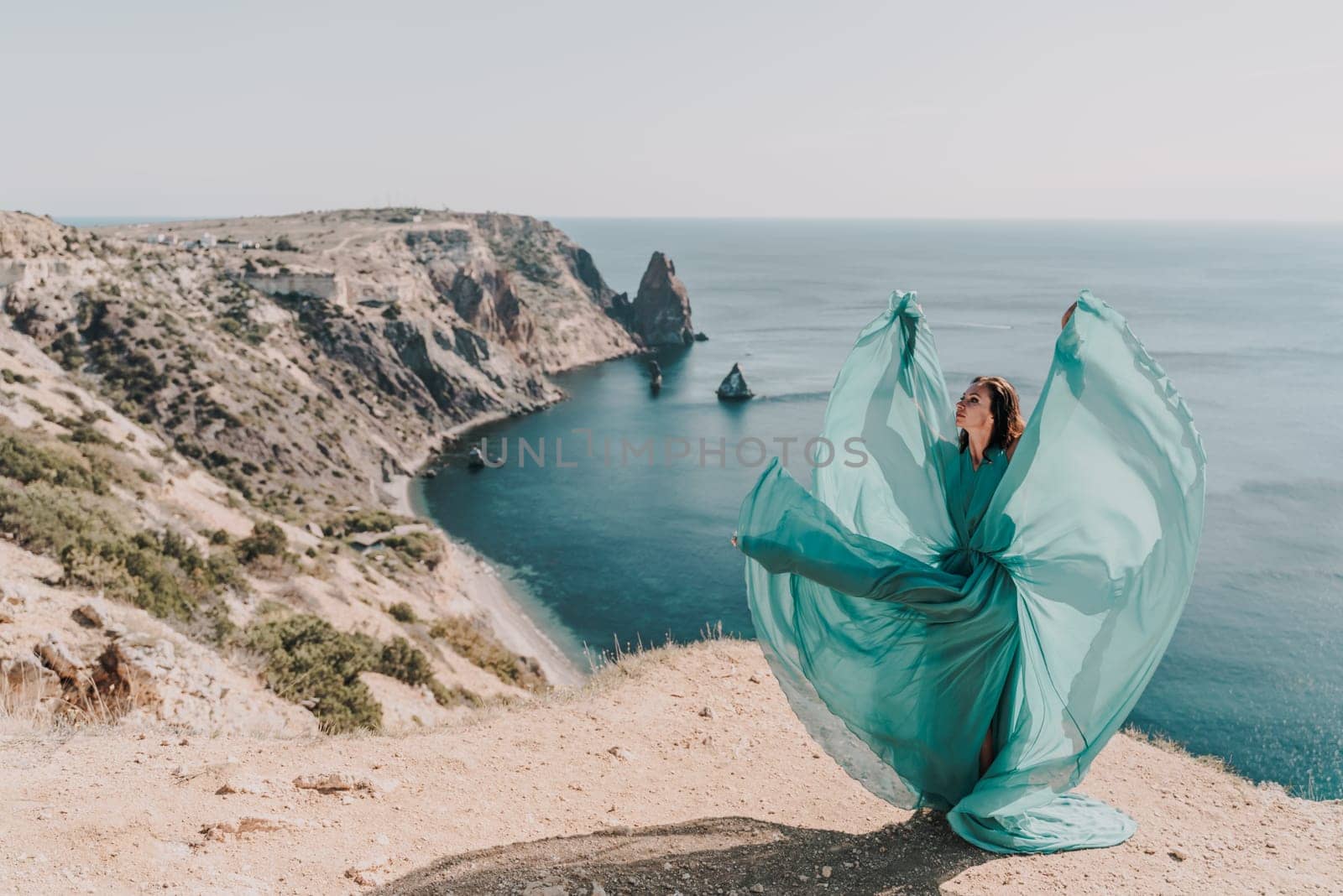 Woman green dress sea. Female dancer posing on a rocky outcrop high above the sea. Girl on the nature on blue sky background. Fashion photo